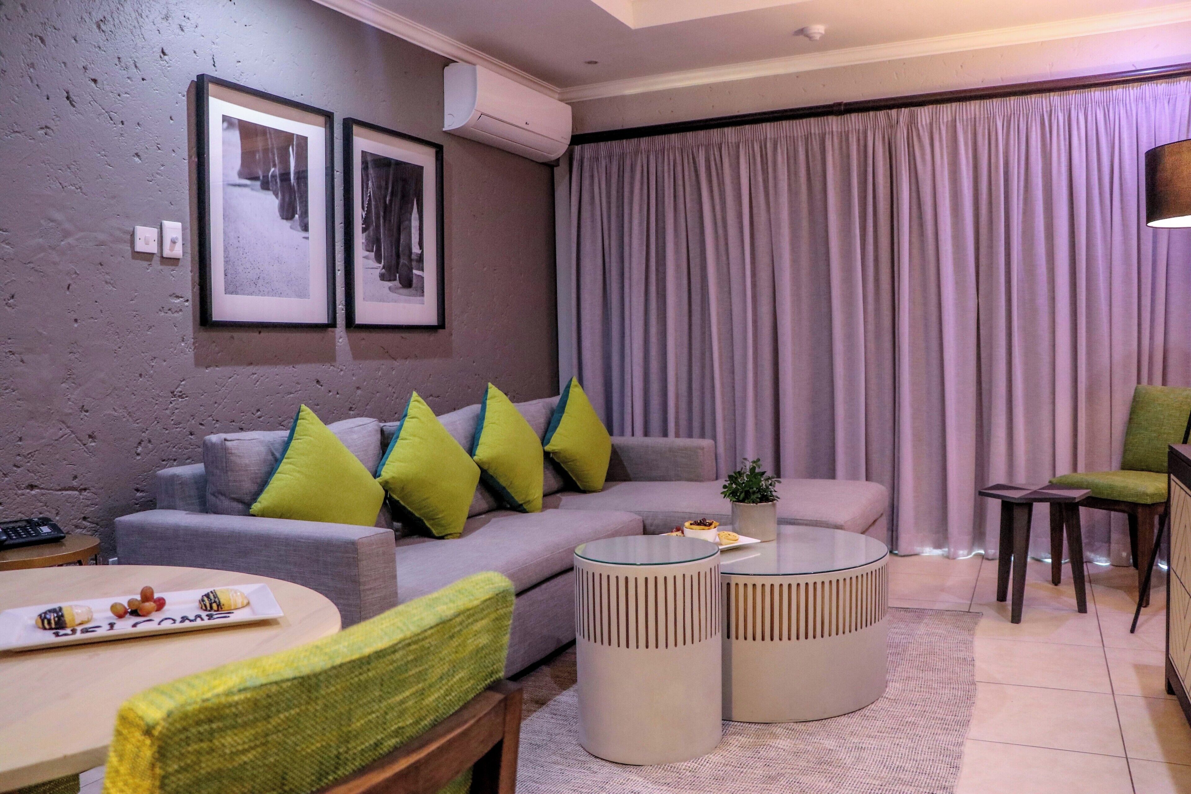 Ein modernes Wohnzimmer mit einem grauen Sofa, grünen Kissen, einem runden Couchtisch und einem grauen Sessel.