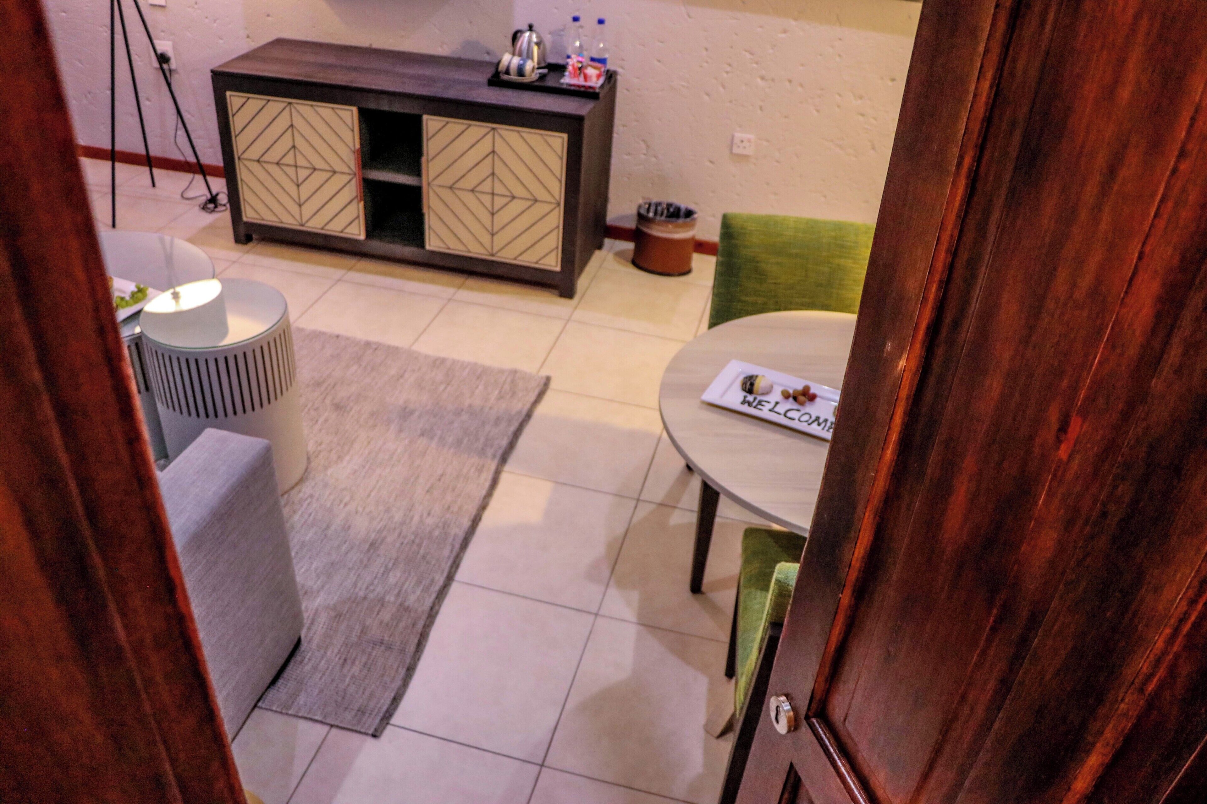 A room with a round table, a cabinet with geometric patterns, a grey rug, and a 'WELCOME' sign on the table.