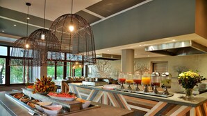 Zona de buffet con diversas opciones de comida, una presentación de frutas y dispensadores de jugo.