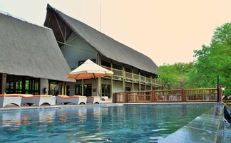 A pool with lounge chairs and umbrellas, a building with a thatched roof, and a wooden deck.