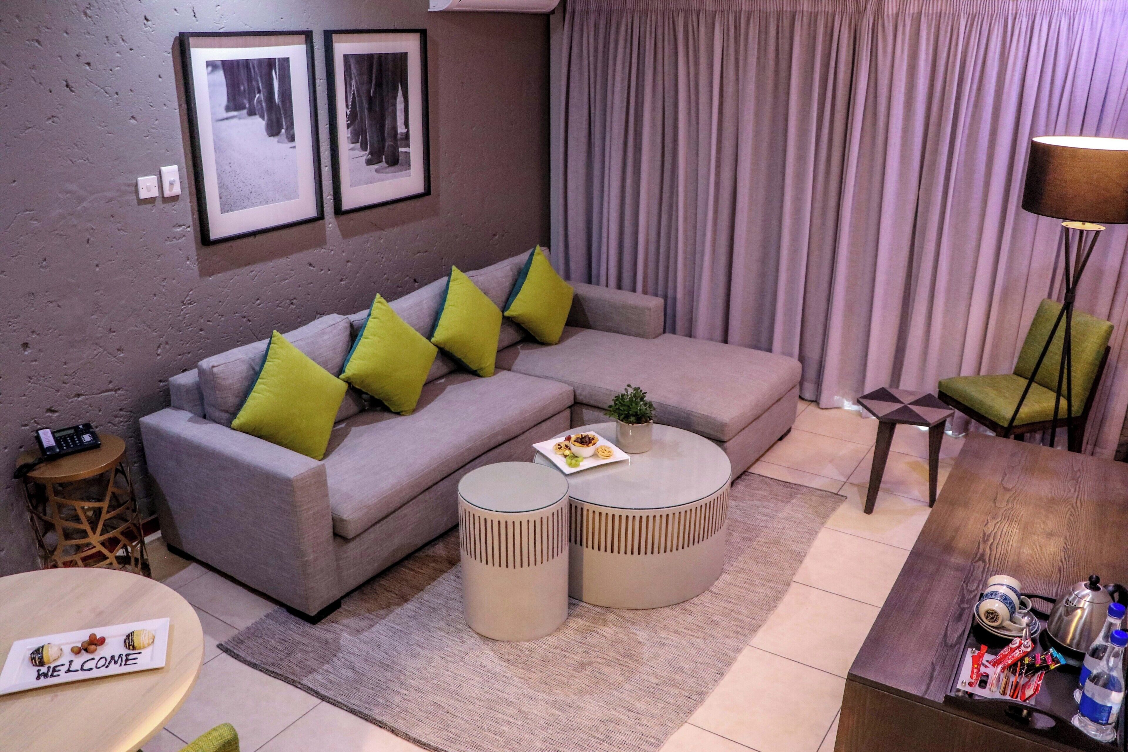 A modern living room with a grey sofa, two round side tables, a coffee table, a lamp, and a small side table with a phone.