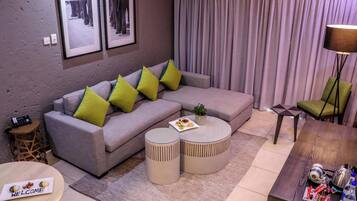 A modern living room with a grey sofa, two round side tables, a coffee table, a lamp, and a small side table with a phone.
