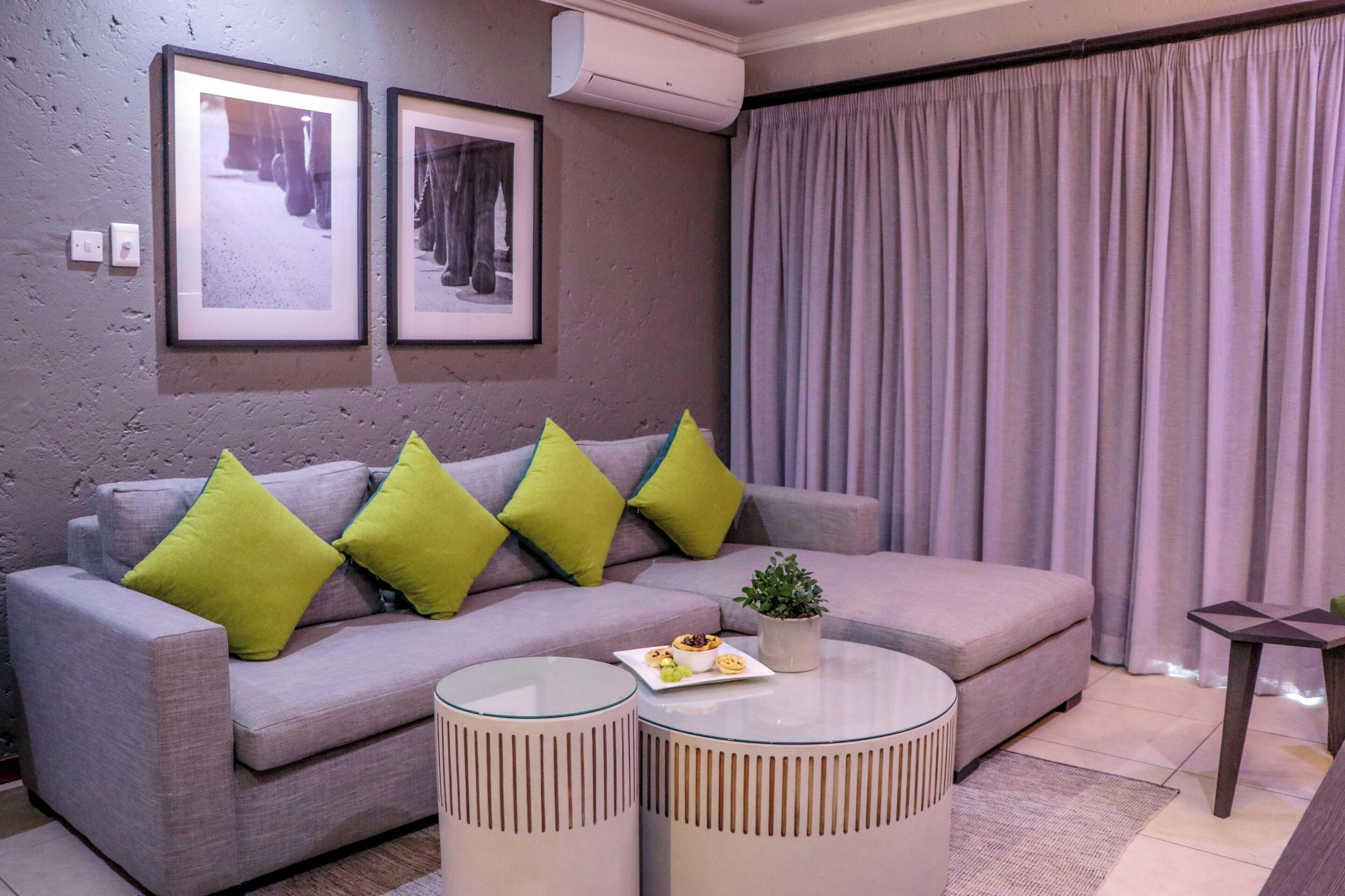 Un salon moderne avec un canapé gris, des coussins verts, une petite table sur laquelle est posée une plante, et deux tableaux encadrés accrochés au mur.