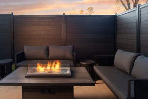 Un área de estar al aire libre con una chimenea, asientos acolchados y vistas al cielo.