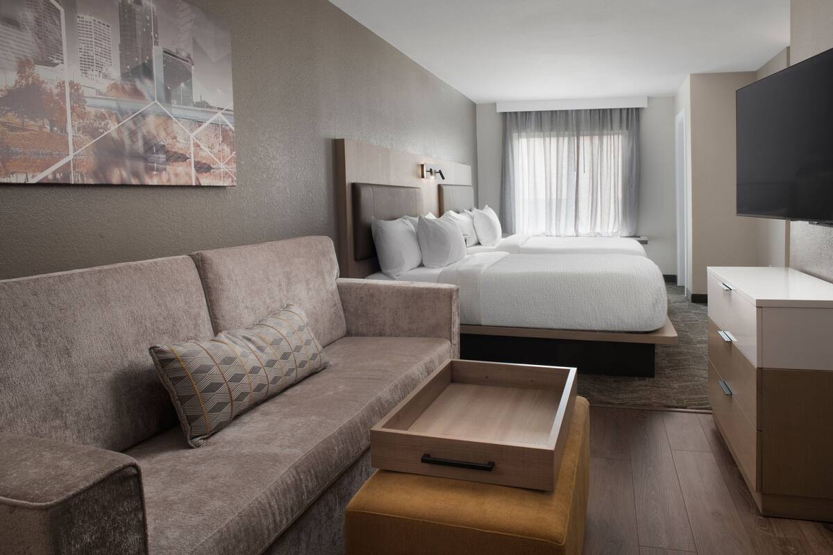 A modern hotel room with a sofa, a bed, a TV, and a painting on the wall.