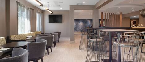 A modern hotel lobby with a bar area, seating arrangements, and a large wall-mounted TV.