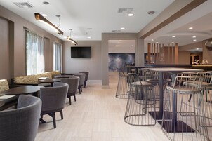 Un moderno hall de hotel con zona de bar, arreglos de asientos y un televisor grande montado en la pared.