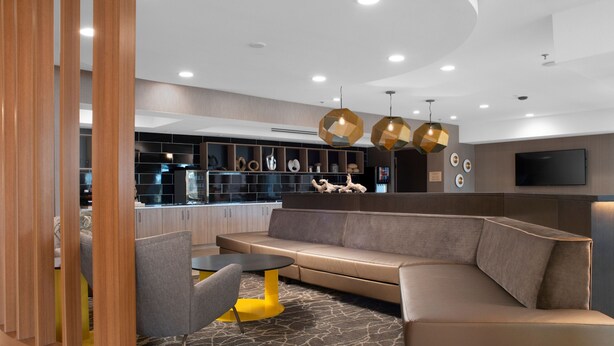 A modern living area with a sectional sofa, a small round table, and a wooden partition. - Springhill Suites Marriott Little Rock West (Little Rock)