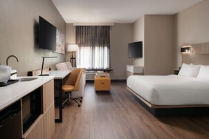 Una habitación de hotel con cama, escritorio, silla y televisor montado en la pared.