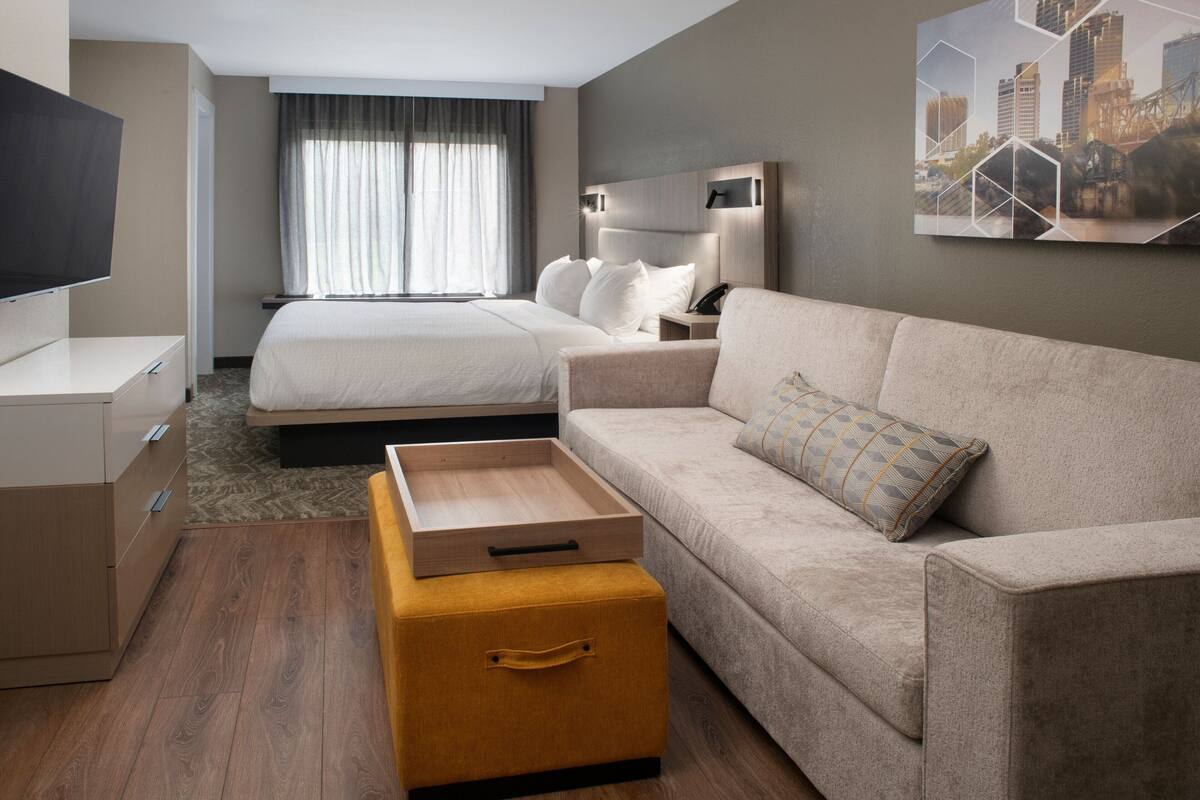 A hotel room with a bed, a sofa, a TV, a desk, and a drawer unit.
