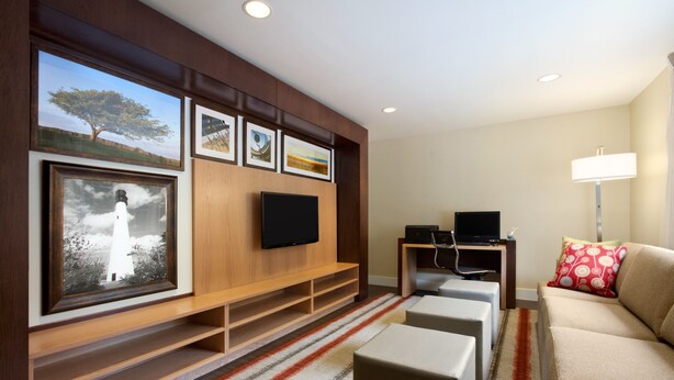 A modern living room with a flat-screen TV, a sofa, a coffee table, and a TV stand with framed pictures. - MainStay Suites Detroit Farmington Hills (Farmington Hills)