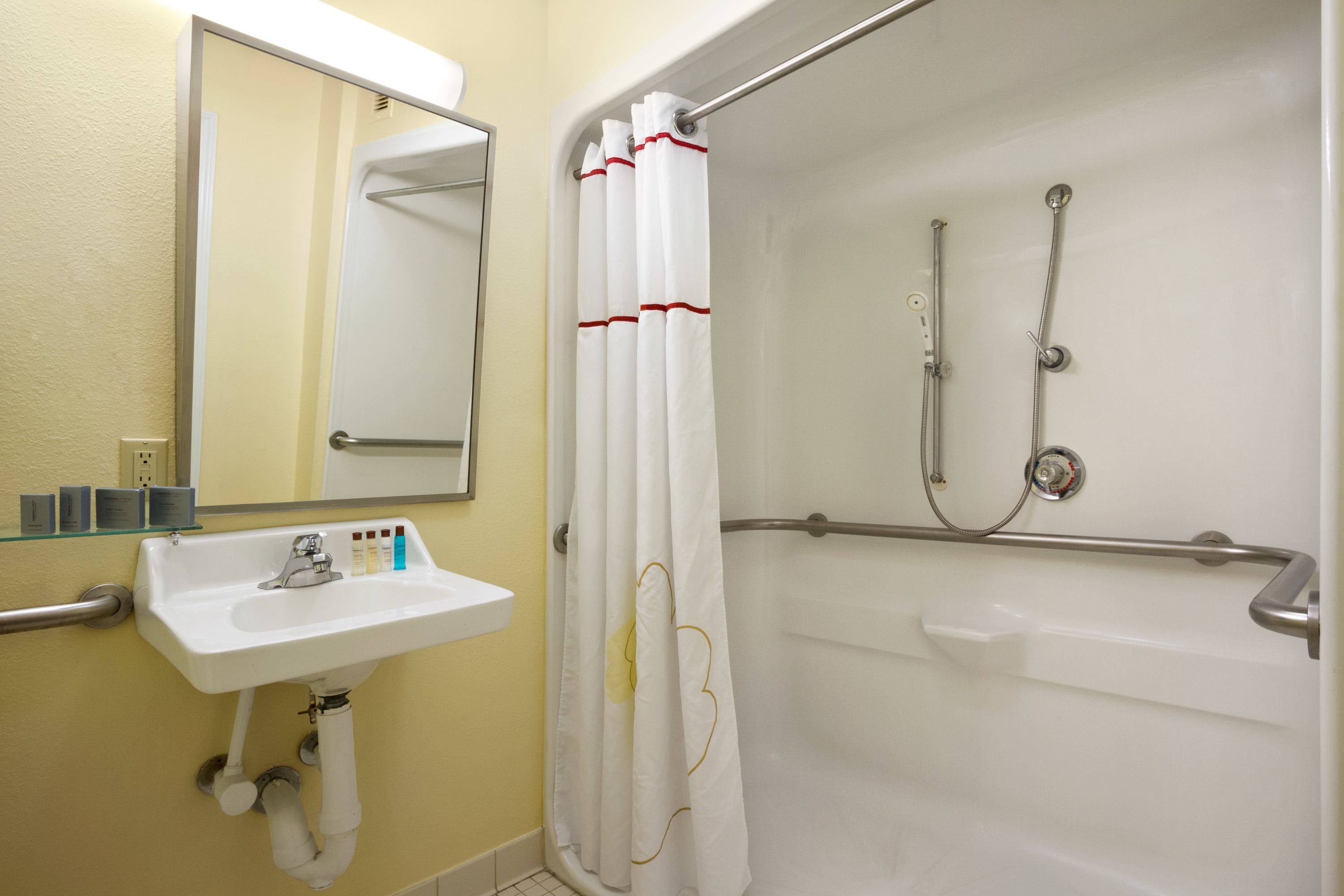 Un baño con lavamanos blanco, espejo y ducha con cortina blanca.