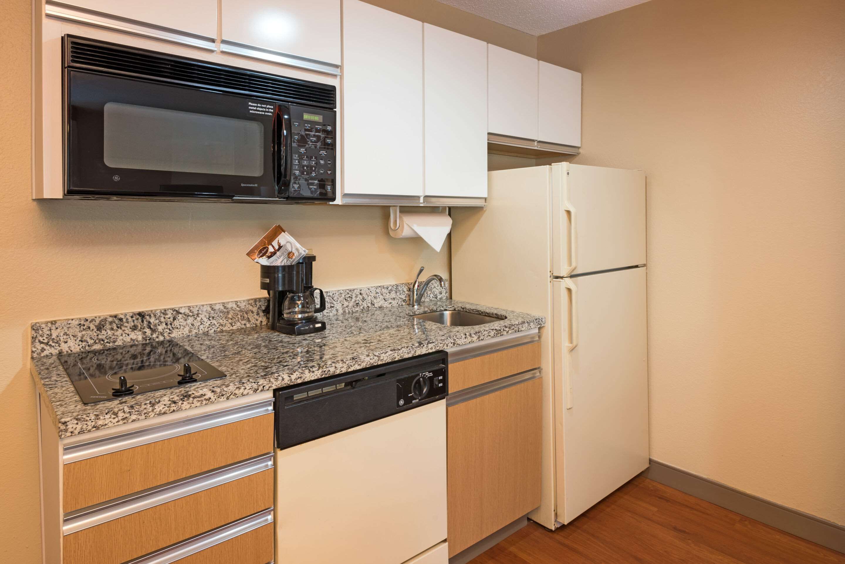 Cocina compacta con microondas integrado, refrigerador, lavavajillas y encimera de granito.
