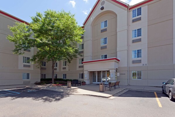 A multi-story building with a parking lot, a tree, and outdoor seating. - MainStay Suites Detroit Farmington Hills (Farmington Hills)