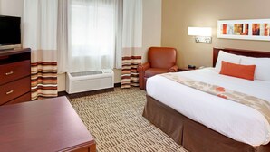 A hotel room with a bed, a desk, a chair, a TV, an air conditioner, and a wall-mounted lamp. - MainStay Suites Detroit Farmington Hills (Farmington Hills)