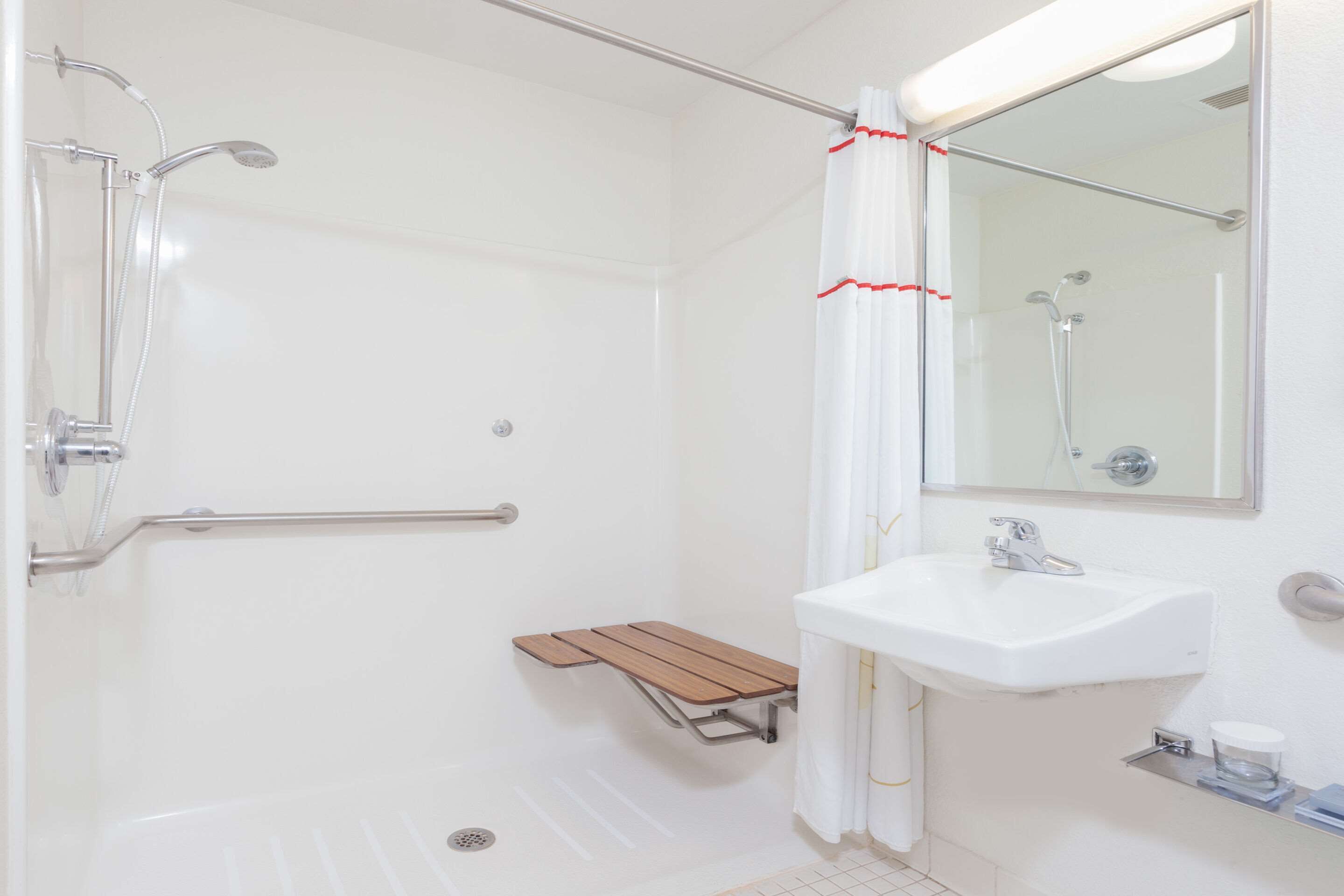 A bathroom with a shower, a sink, a mirror, and a wooden bench.