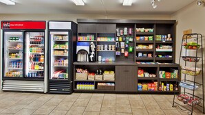 Una estación de autoservicio para bebidas con Coca-Cola y otras opciones, una máquina de café, y una variedad de aperitivos y productos de alimentación.