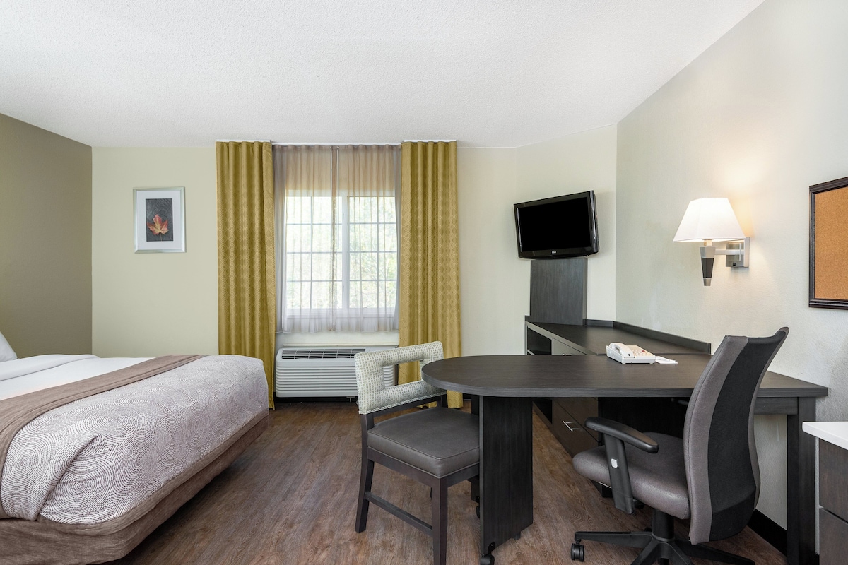 Habitación de hotel con cama, escritorio, silla, televisor y teléfono.