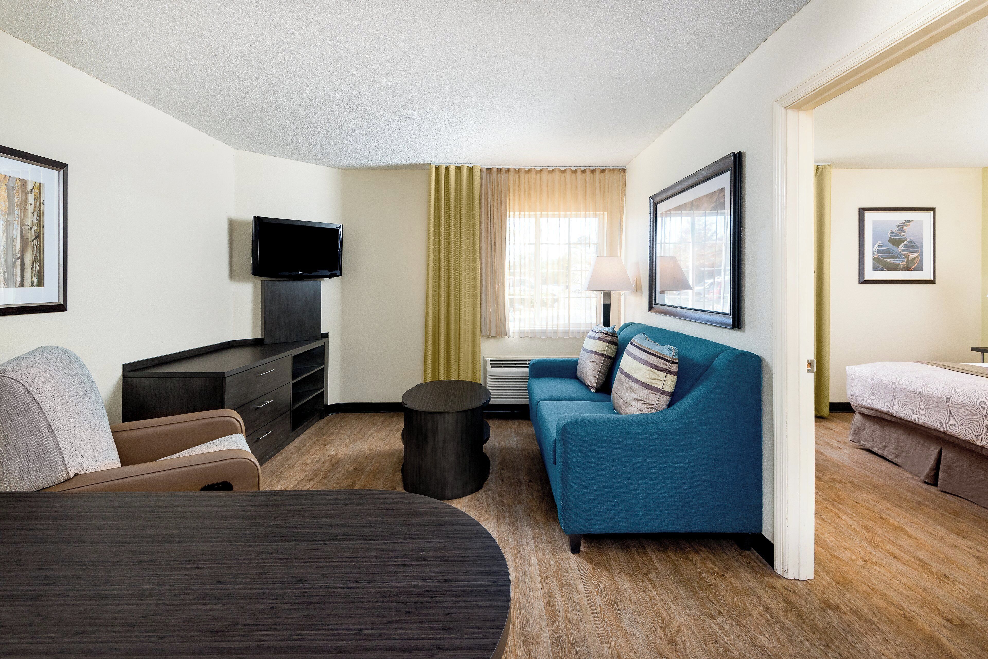 Habitación de hotel con cama, sofá, televisión, una mesita y ventana con cortinas.
