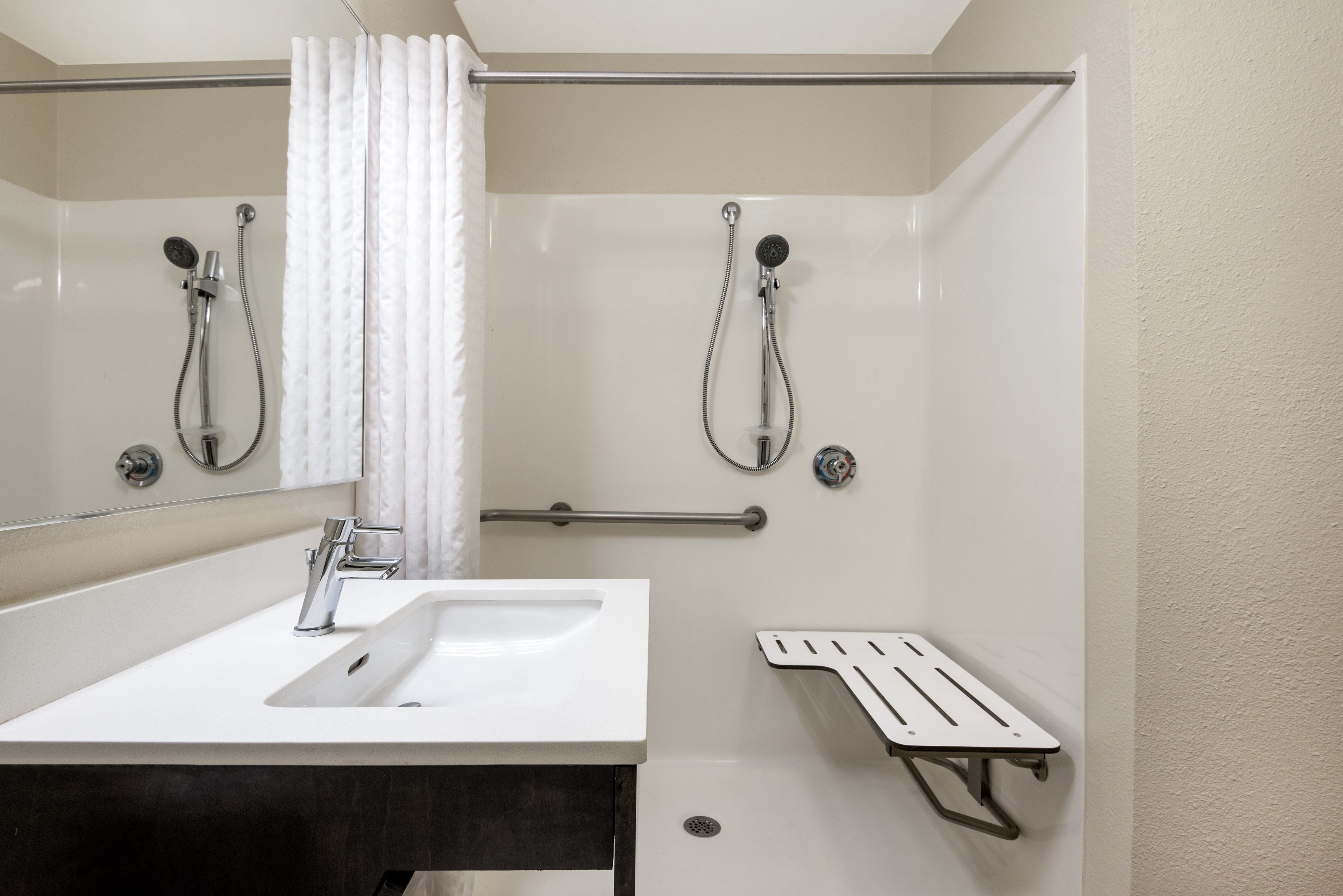 A modern bathroom with a white sink, two showerheads, a towel rack, and a grab bar.