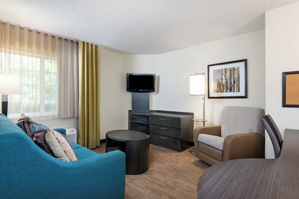 A modern hotel room with a flat-screen TV, a sofa, a chair, a small table, and a painting on the wall.