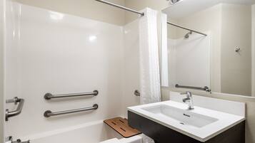Un baño moderno con una bañera blanca, un lavabo con encimera oscura y un espejo sobre el lavabo.