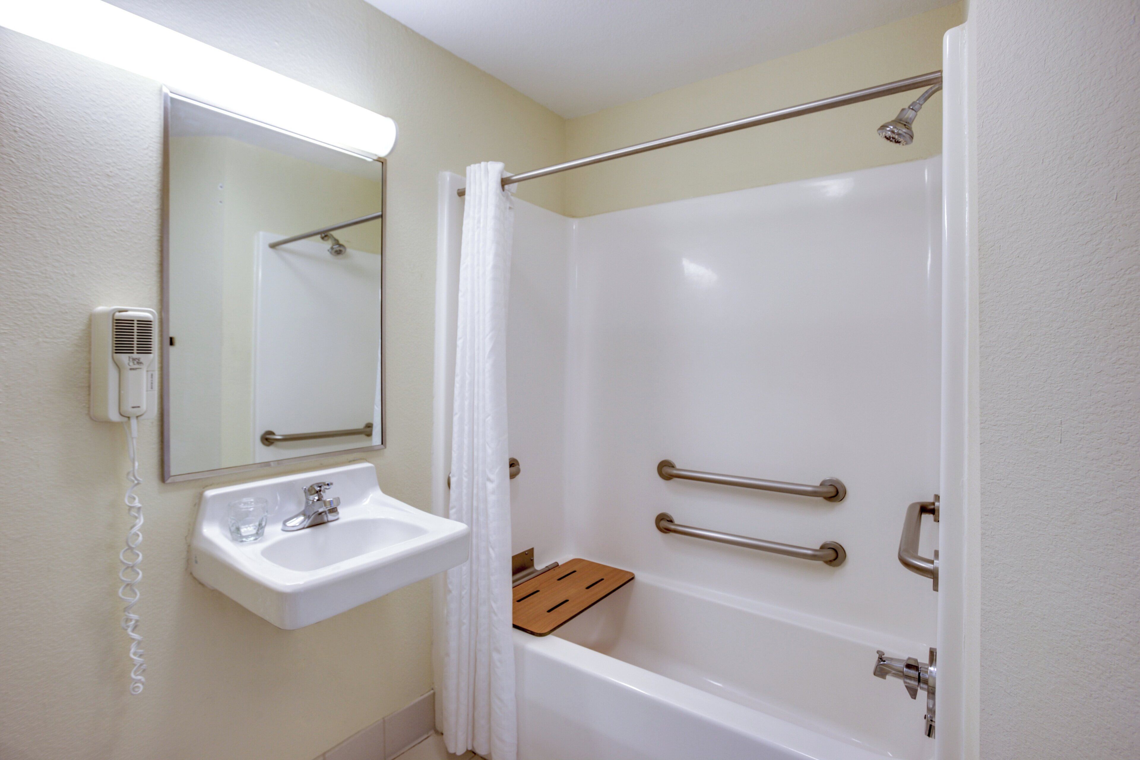 A bathroom with a white sink, a mirror, a handheld showerhead, and a bathtub.