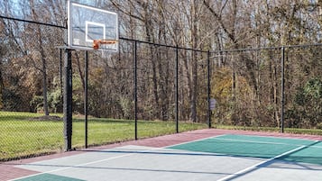 An outdoor basketball court with a chain-link fence, a basketball hoop, and a warning sign.
