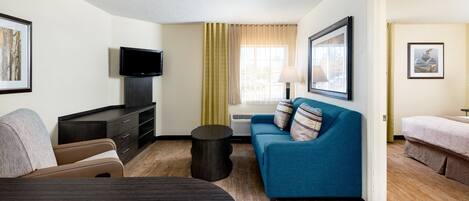 A hotel room with a sofa, a TV, a small table, and a bed.