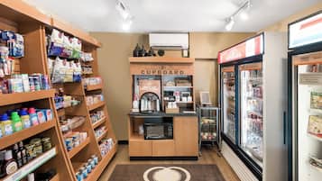 Habitación de hotel con kitchenette, que incluye una cafetera, un refrigerador con bebidas y estantes con aperitivos y artículos de aseo.