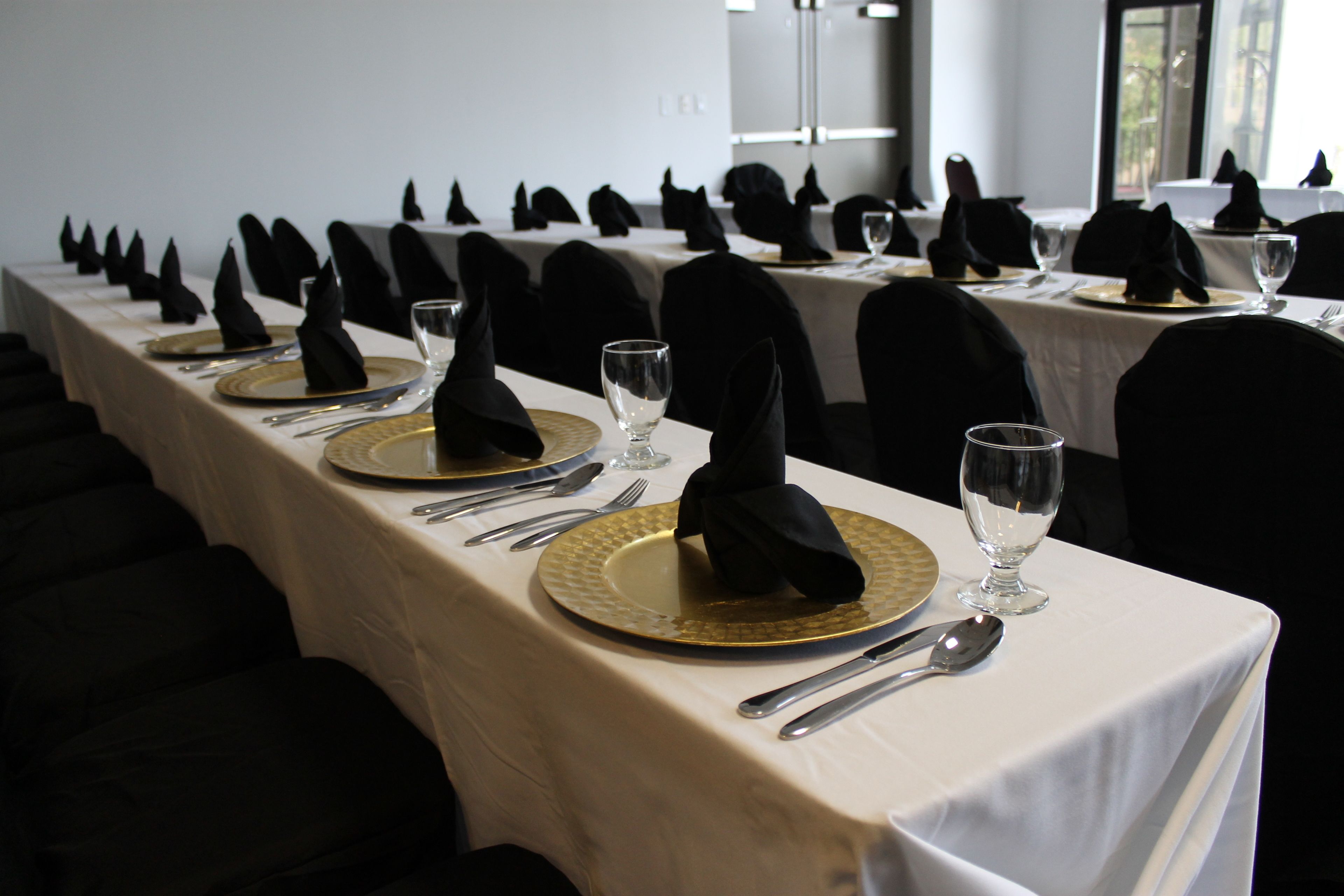 A long dining table with black napkins, gold plates, and silverware, set for a formal meal.