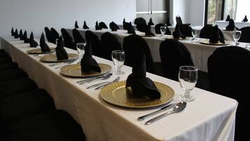 A long dining table with black napkins, gold plates, and silverware, set for a formal meal.