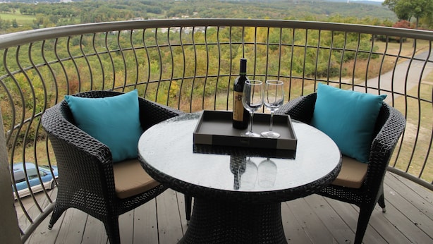Une table ronde avec deux chaises sur un balcon, une bouteille de vin et deux verres.