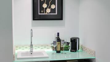 A modern kitchen with a glass countertop, a sink, a framed artwork, and a coffee machine.