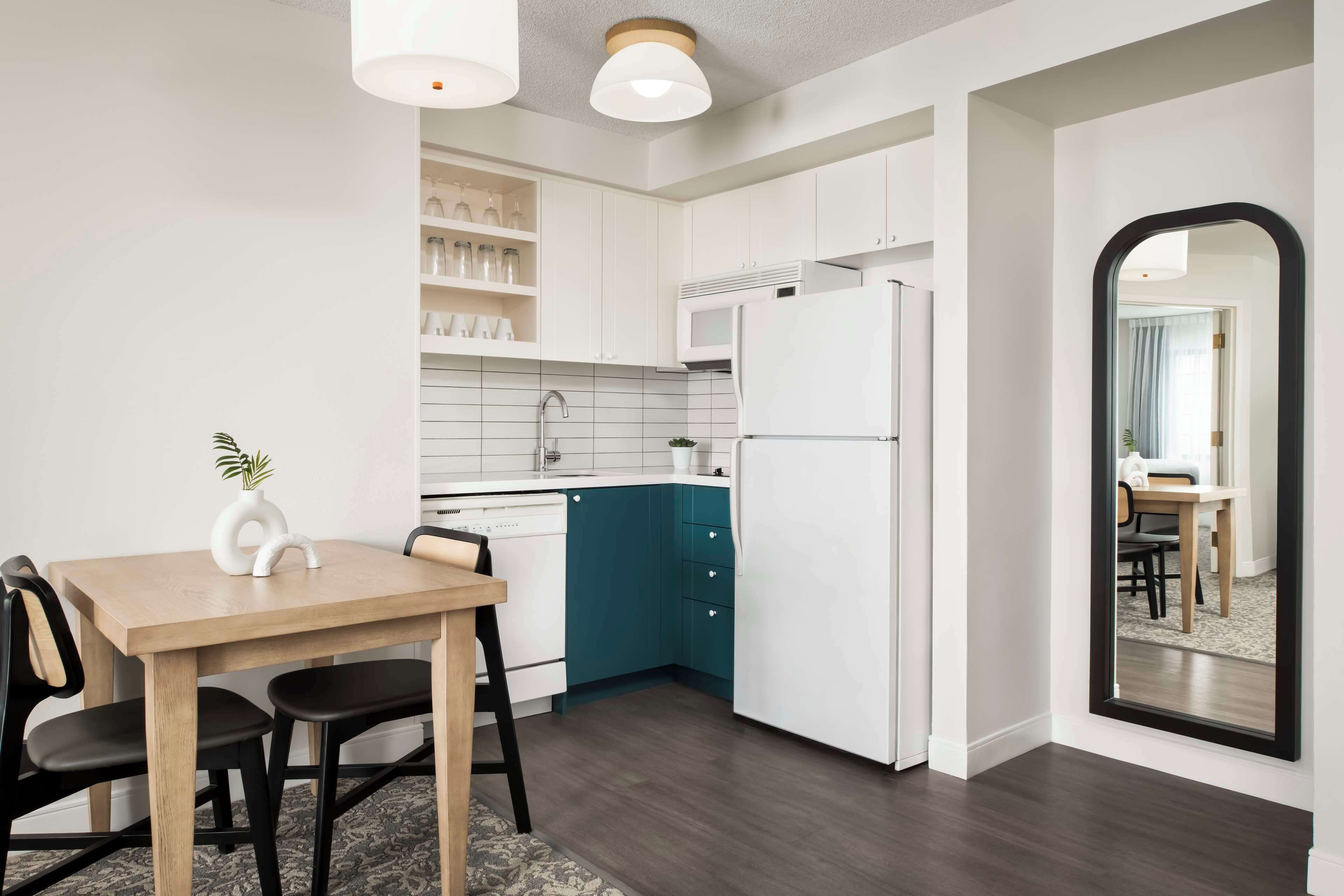 Eine moderne Küche mit weißen Schränken, einer Wand in Türkis, einem weißen Kühlschrank und einem Essbereich mit einem Holztisch und Stühlen.
