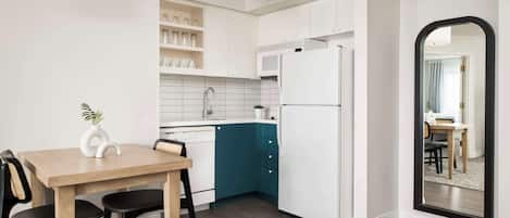 Eine moderne Küche mit weißen Schränken, einer Wand in Türkis, einem weißen Kühlschrank und einem Essbereich mit einem Holztisch und Stühlen.