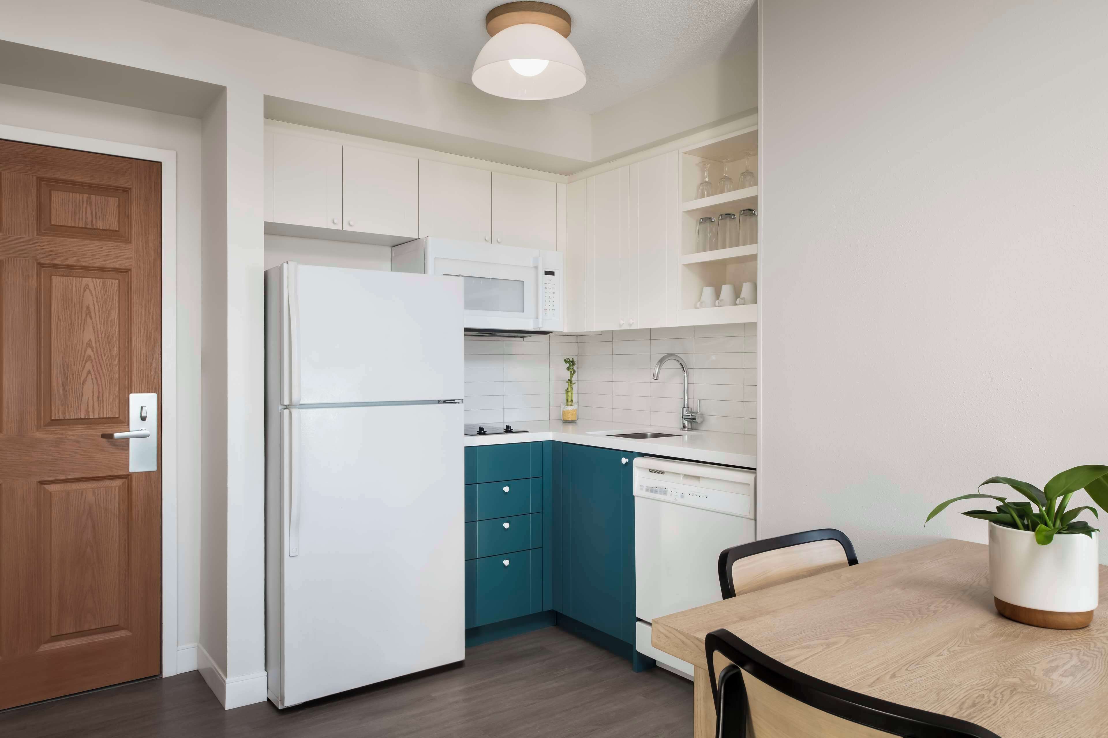 Una cocina moderna con armarios blancos, un refrigerador blanco, un microondas, un lavavajillas y una mesa de comedor con sillas.