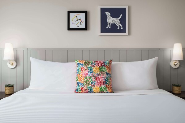 Una cama bien hecha con sábanas blancas, una almohada colorida y dos lámparas fijadas a la pared.