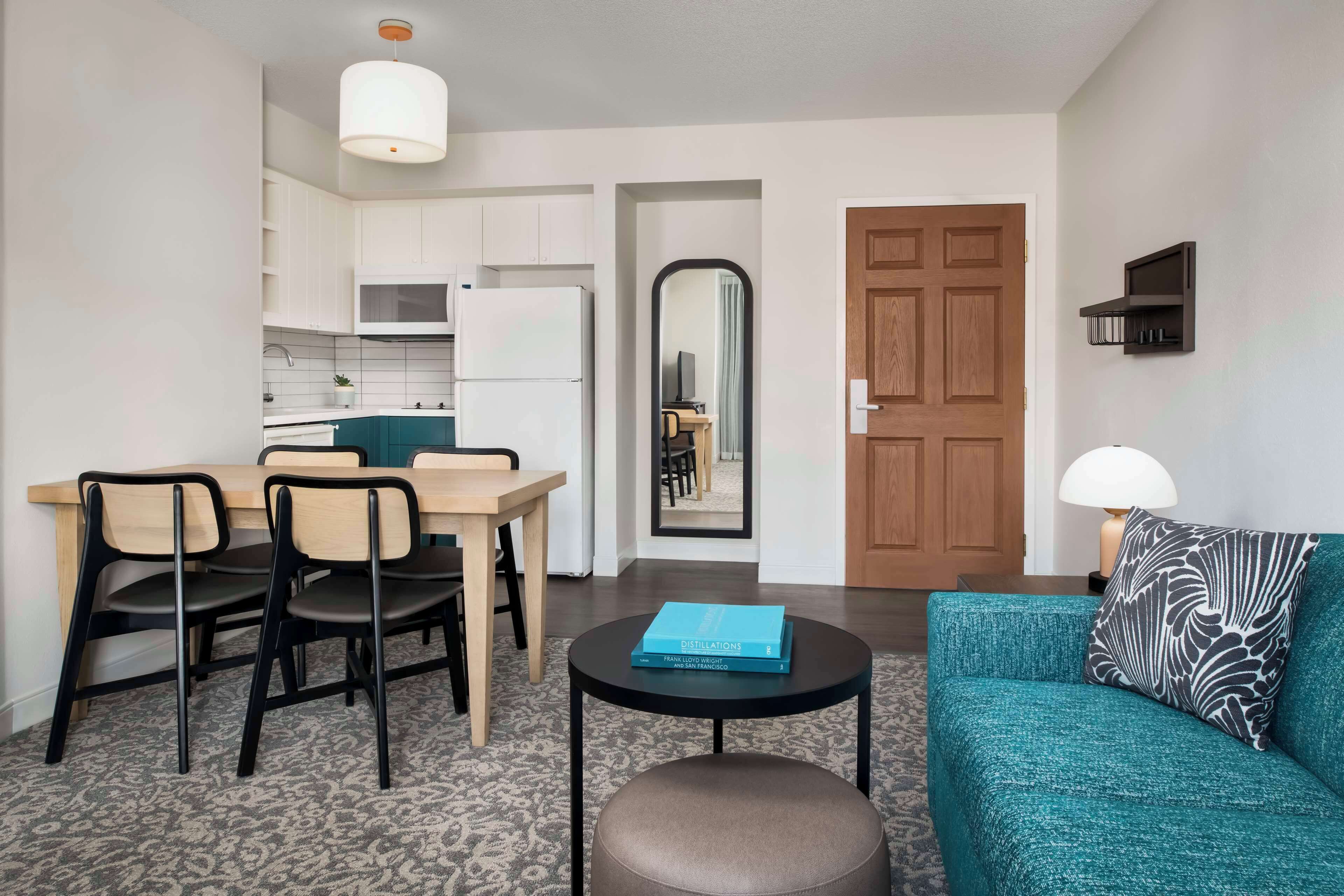 Un salon moderne avec un canapé de couleur turquoise, une table basse et un coin repas comprenant une table et des chaises en bois.