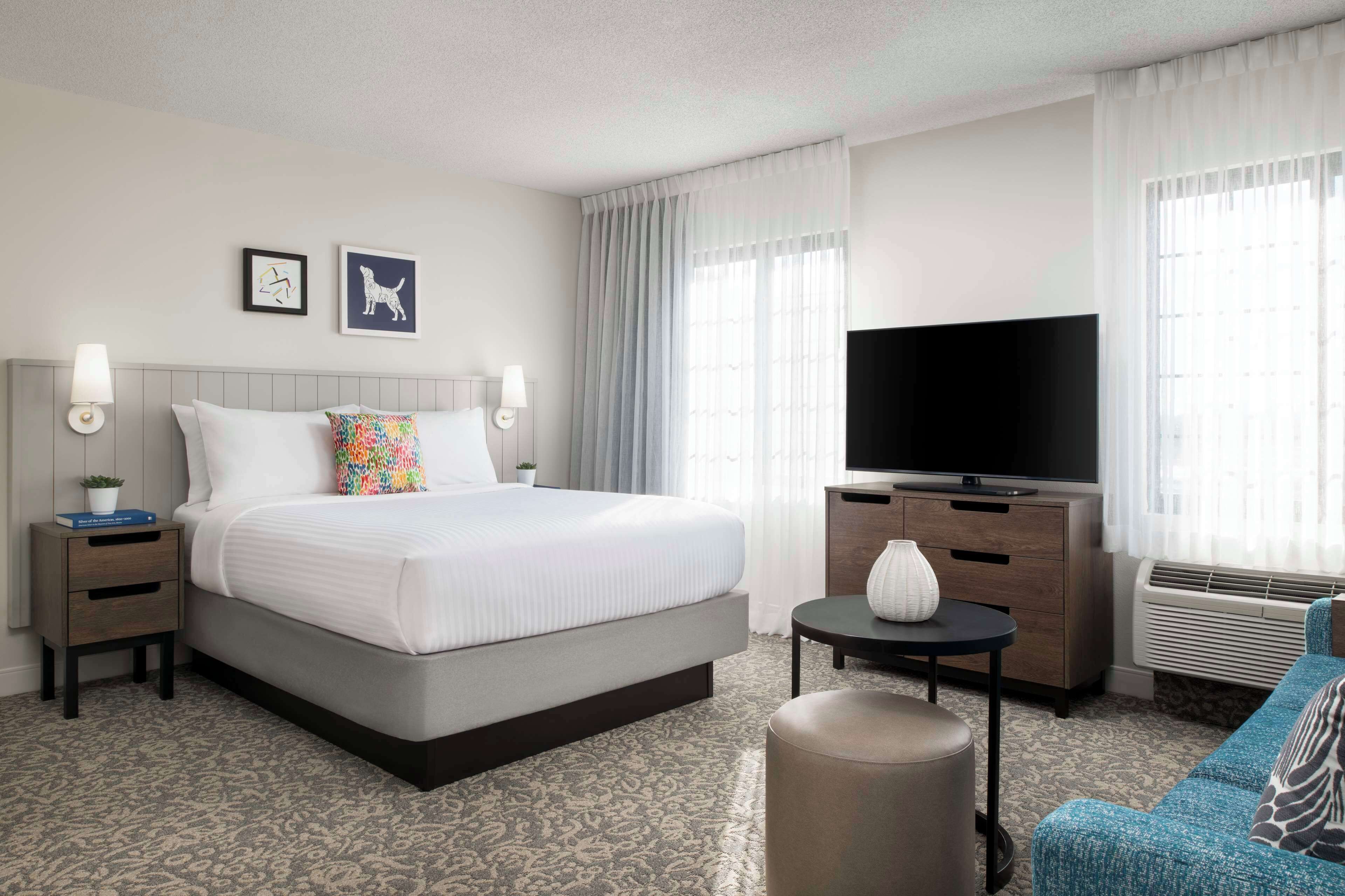 A hotel room with a large bed, a flat-screen TV, a small table, a sofa, and a nightstand.