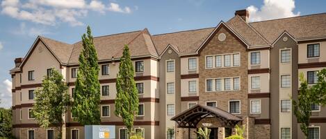 A multi-story hotel with a central entrance, surrounded by well-maintained lawns and trees.