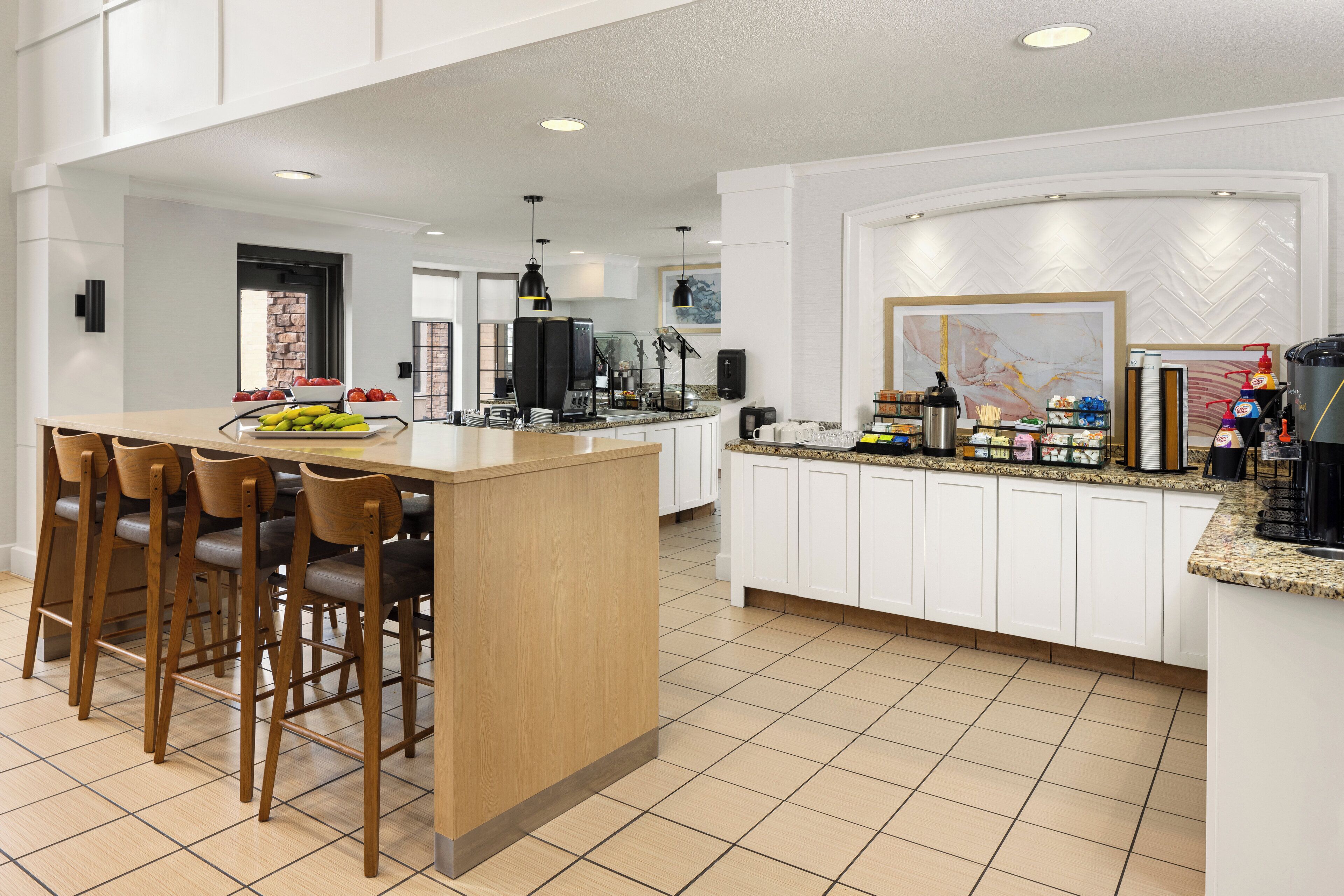 Una cocina moderna con una isla central, taburetes de bar, armarios blancos y piso de baldosas.