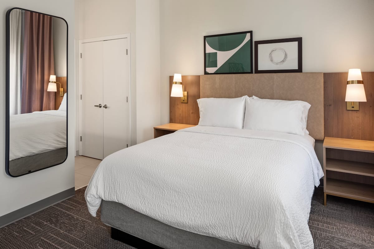 A hotel room with a large bed, a wooden headboard, two bedside tables with lamps, a mirror, and a door.