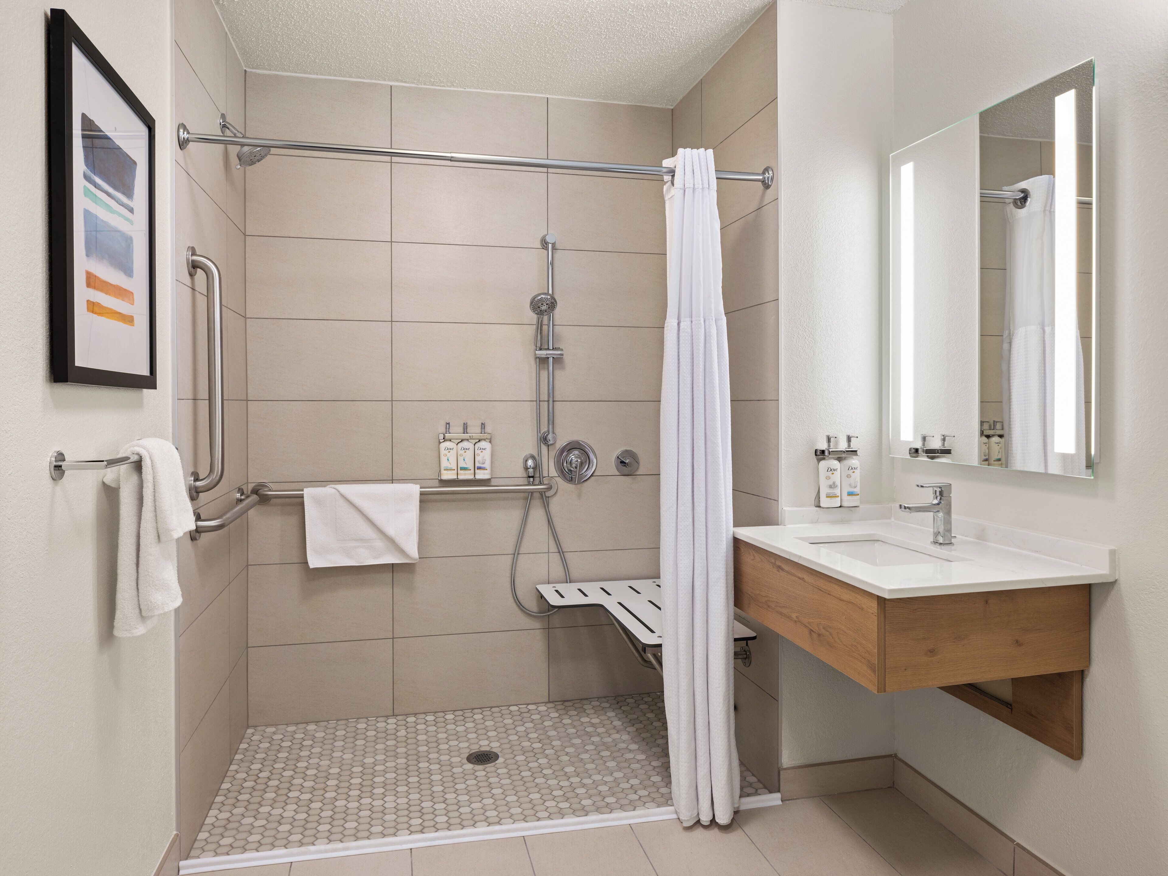 Un baño moderno con ducha, tocador con espejo y un cuadro en la pared.
