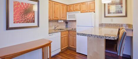 A compact kitchen with wooden cabinets, a white refrigerator, and a granite countertop.