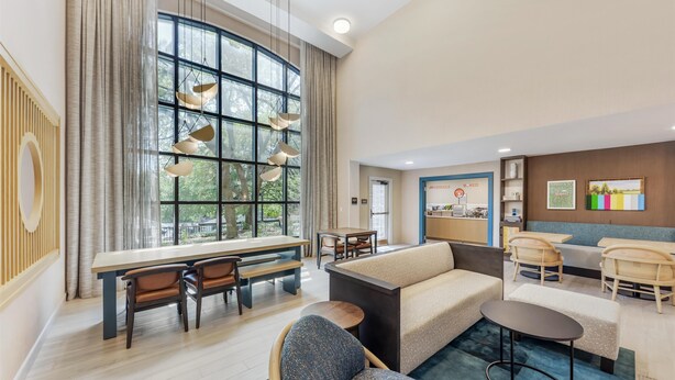 A spacious hotel lobby with a large window, a seating area with sofas and chairs, a dining table, and a reception desk. - Sonesta ES Suites Austin The Domain Area (Austin)