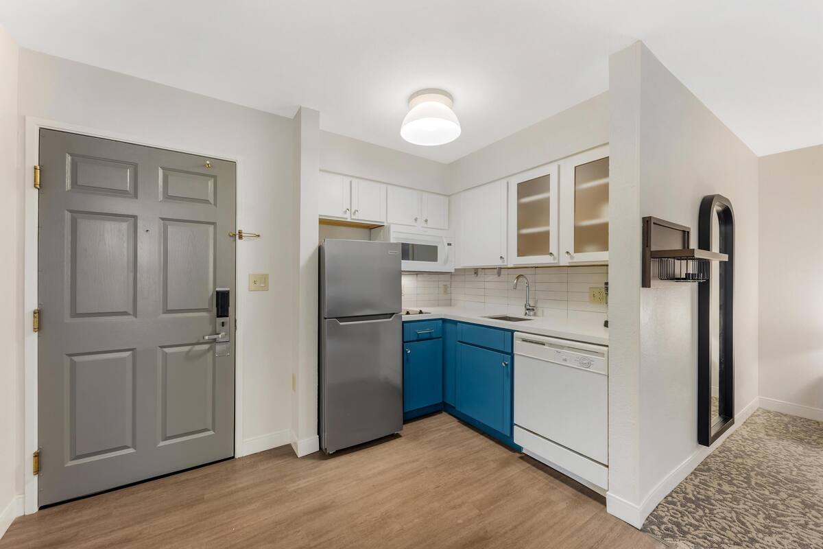 A kitchen with white cabinets, a blue countertop, a stainless steel refrigerator, and a microwave.