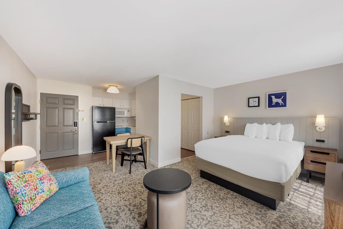 A hotel room with a bed, a desk, a chair, a lamp, and a small table.