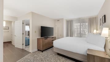 A hotel room with a large bed, a TV on a wooden dresser, a door leading to a bathroom, and a window with curtains.