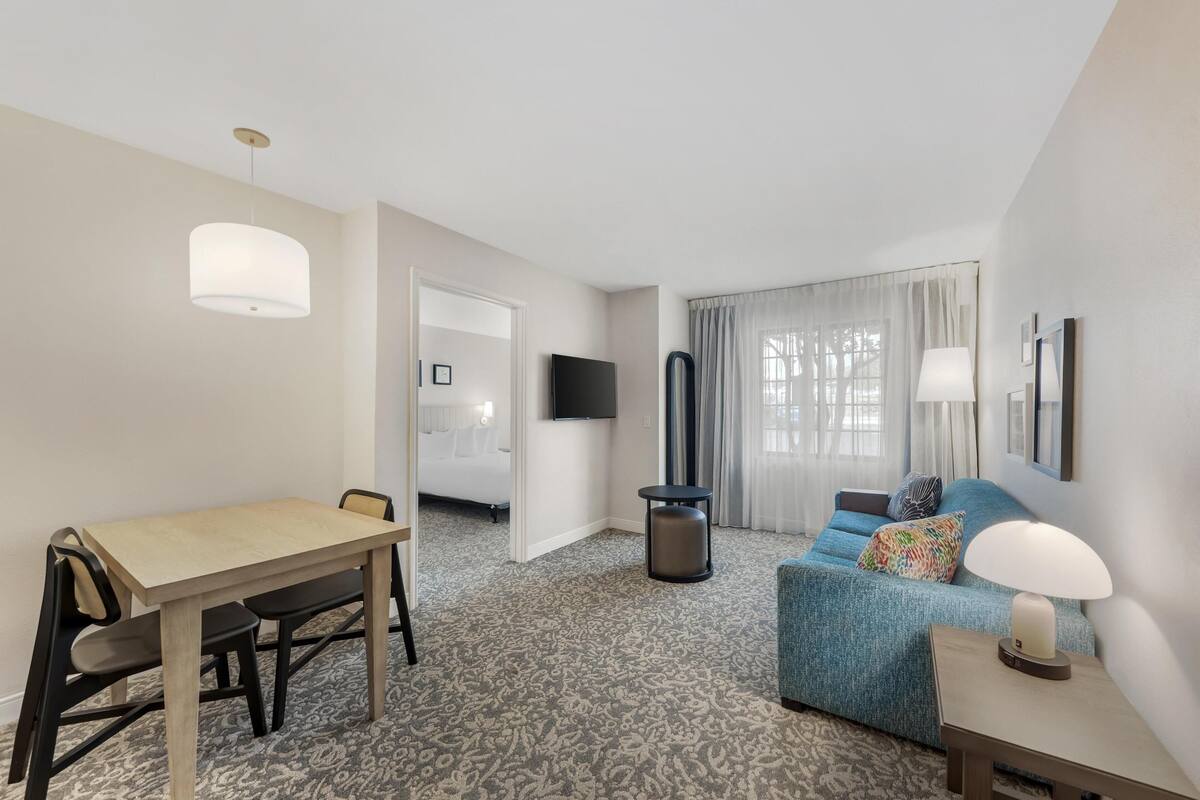 A hotel room with a dining table, a sofa, a TV, and a lamp.